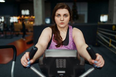 超重的女人在健身房锻炼自行车图片