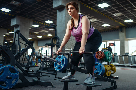 超重的女人在健身房的酒吧里锻炼图片