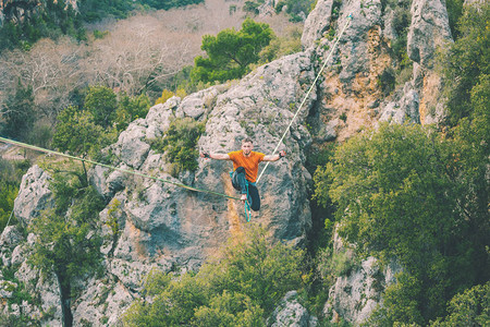 高线山脉的背景一个人坐在拉长的吊索上走钢丝的表演Highliner在深渊上保持平衡运动员摔倒背景图片