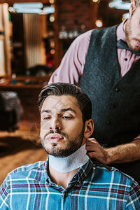 理发师在英俊的大胡子男人脖子上固定衣领图片
