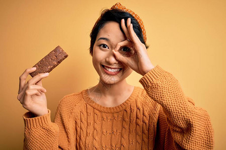 年轻美丽的亚洲女孩拿着谷物能量蛋白棒图片