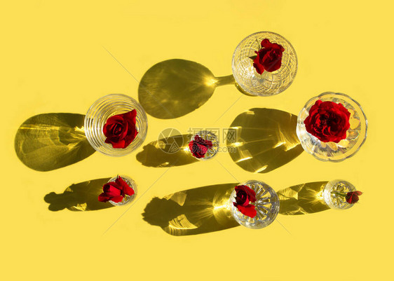 带有清澈水和红玫瑰的眼镜站在黄色背景上图片