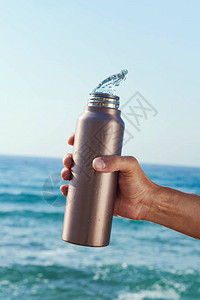 在海洋前从铝再用水瓶里倒水的人图片