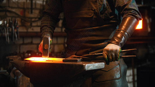 在车间工作的铁匠男子用锤子击打热图片