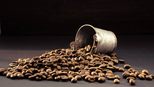 带咖啡的装饰金属桶棕色颗粒溢出在深色表面上新鲜烘焙咖啡豆的背景图片