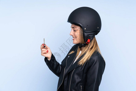 年轻金发女金发美女戴着摩托车头盔和钥匙超过孤背景图片