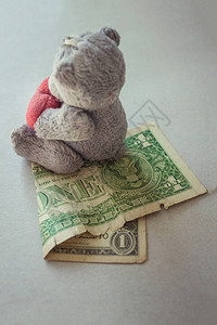 一只小玩具泰迪熊坐在一美元上图片