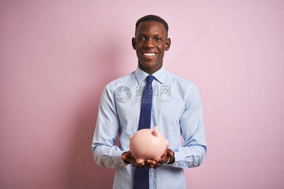 非洲裔美国商人拿着存钱罐站在孤立的粉红色背景上图片