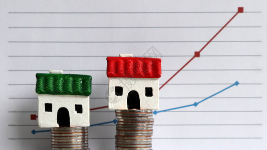 线图前两堆硬币上的两个微型房子房价上涨与贫富差距之图片
