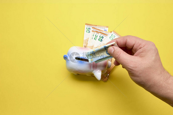 将钱放进粉红猪钱箱的人在黄色背景上储蓄图片