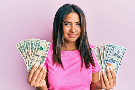 年轻拉丁女孩拿着一无所知的美元困惑的表情图片
