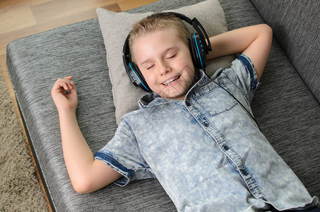 在家听耳机和唱歌的时髦小男孩快乐地笑着男孩在家里沙发上休息图片