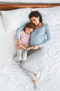 爱怀孕的妈在床上一起休息时给小女儿看书的顶图片