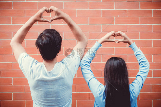 年轻的亚裔夫妇在爱中快乐在砖底的手心形状图片