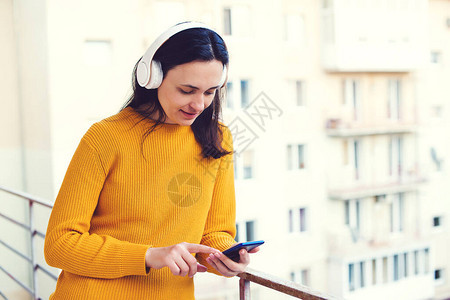 冠状隔离女人在阳台听音乐使用手机和无线耳机的女人在家自我隔离戴着耳机在阳台上呼吸新鲜空气的女图片