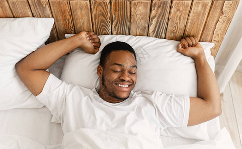休息的非洲裔美国人早上醒来伸展双手醒来躺在家里的床上图片