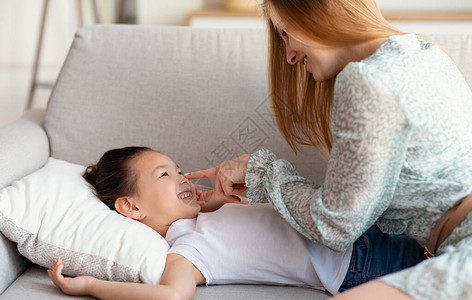 快乐的妈抚摸小鼻子女孩一起在沙发家玩得开心地欢笑着图片