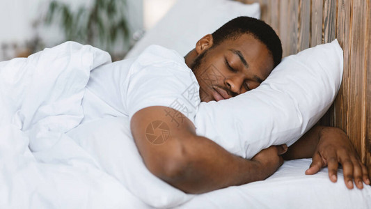 非裔美国人睡觉时用手抱枕头和眼睛睡在舒适的床上图片