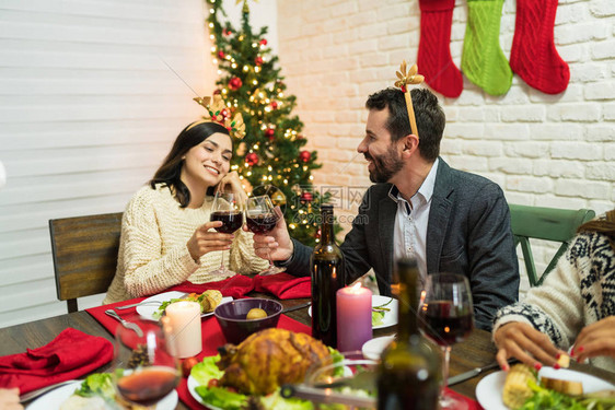 欢笑的男女在圣诞节在家餐桌旁聊天时在图片