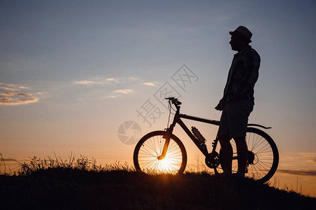 在日落背景上骑自行车的时髦男人的剪影身体活动和健康生活方式图片