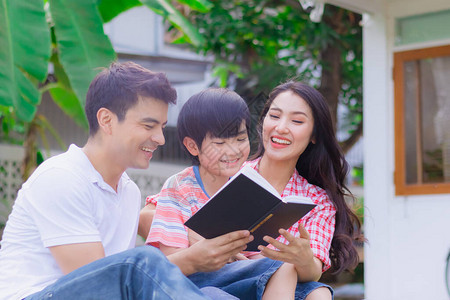快乐的家庭父亲母亲和儿子在家里的院子里一起读书作为活动父母和孩子之间的幸福关系或纽带享受图片