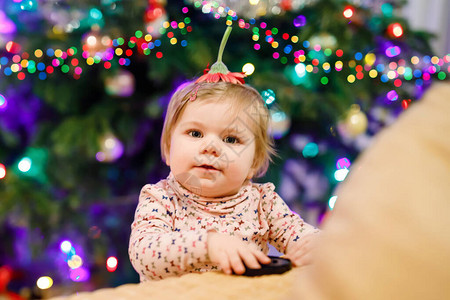 和站立的小可爱女婴的画像圣诞树和背景灯可爱的蹒跚学步的女孩在家穿着便服的图片