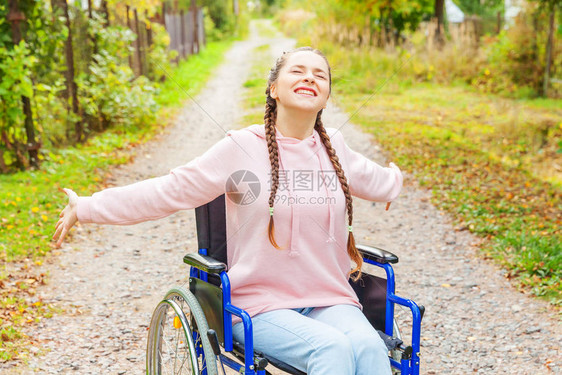 坐在轮椅上的年轻快乐残疾妇女在医院公园的道路上享受自由瘫痪的女孩坐在户外的残疾人无效椅子图片