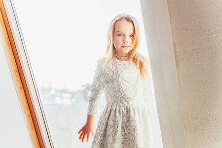 留在家里保持安全穿着白色连衣裙的可爱甜美微笑小女孩站在家里明亮的客厅的窗台上童年学童图片