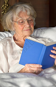 穿着睡衣戴眼镜的老年妇女坐在枕头对着枕头趴在床上读图片