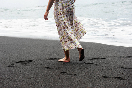 赤脚女人走在水边的黑沙滩上图片