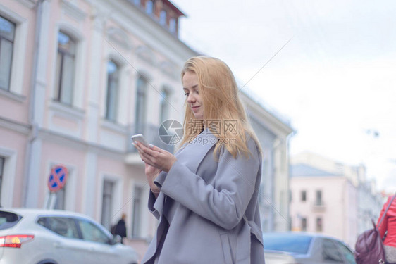 穿着大衣红头发的女孩在市街的智能手图片