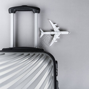 平铺灰色手提箱用灰色背景的小型飞机图片