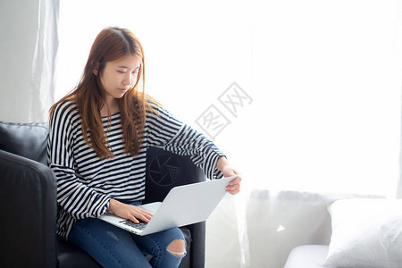 美丽的肖像年轻亚洲女在客厅的椅子上使用笔记本电脑休闲图片