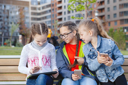 三个带着智能手机的少女坐在一个夏季城市图片