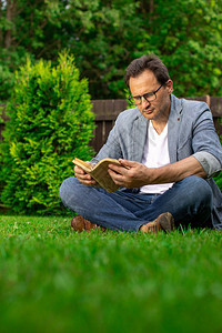 40多位戴眼镜的欧洲男子在夏季日坐在户外的草本阅读书上图片