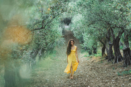 快乐笑容的年轻女人在橄榄树花园里走着黄线夏裙长春图片