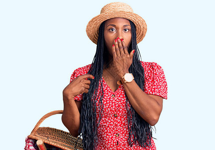穿着暑假帽子拿着野餐篮子的非洲年轻女手拿面包盖住嘴图片