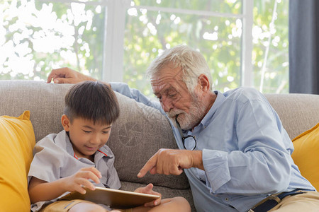 祖父和可爱的小孙子在他们家的沙发上玩触图片