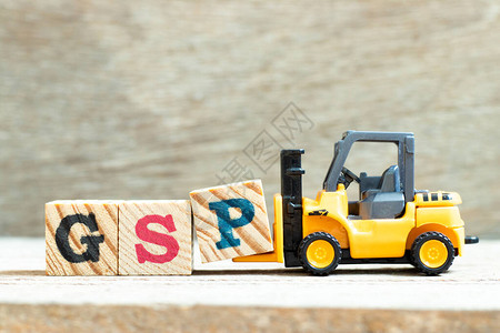 玩具叉车持有字母块P以在木材背景上完成单词GSP图片