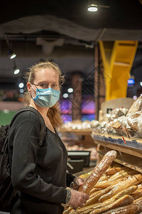 一位戴着蓝色医用口罩和透明手套的年轻女子在超市买面包一个女人穿着一件黑色的毛衣背包戴眼镜的女背景图片