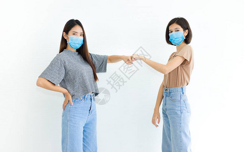 两名身戴卫生面罩的亚洲年轻妇女用拳头打招呼图片