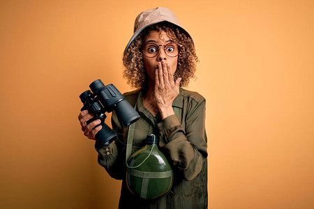 身戴探险帽子和水壶的非洲美旅游妇女拿着双筒望远镜遮住嘴部图片