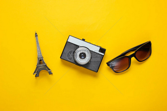 太阳镜反光照相机Eiffel塔黄色背景的雕像旅行背图片