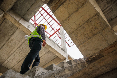 在房屋建筑工地手头戴防护头盔和图纸的年轻专业工程师图片