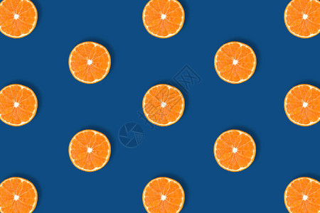 在经典的蓝色背景上分离出的新鲜亮橙色柑橘片的水果图案背景图片
