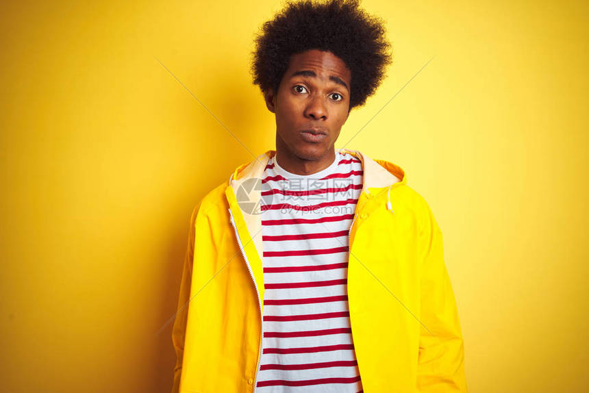 身着雨衣的非洲美国人站在孤立的黄色背景怀疑和紧张之上图片