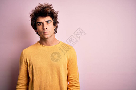 身着黄色散装T恤的英俊男青年站在孤立的粉红背景上站立图片