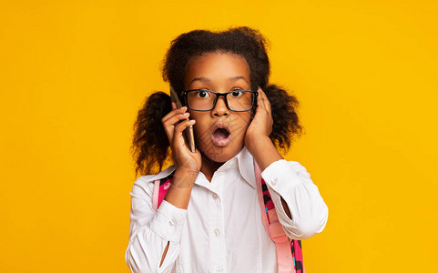 震惊的黑人女孩在电话里用开放嘴透过黄色背景的传言监听声中图片