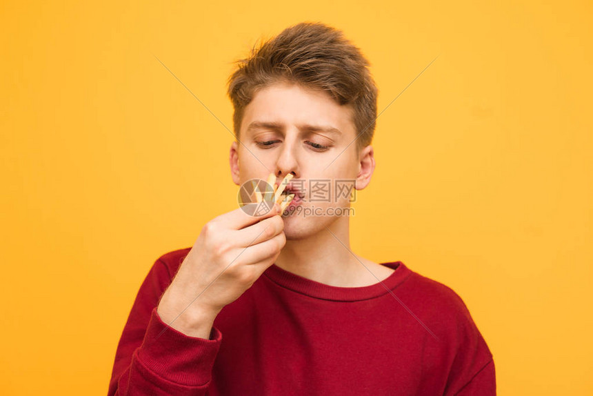 浅色的少年在黄色背景上吃着几条薯图片