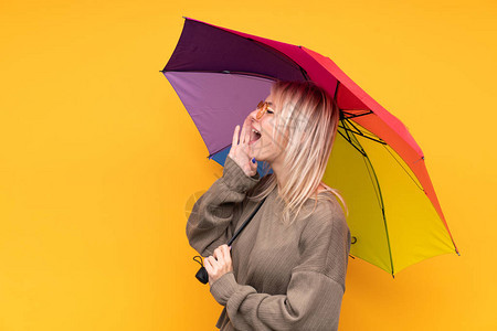 年轻金发女金发女郎拿着雨伞在孤立的黄墙上张图片